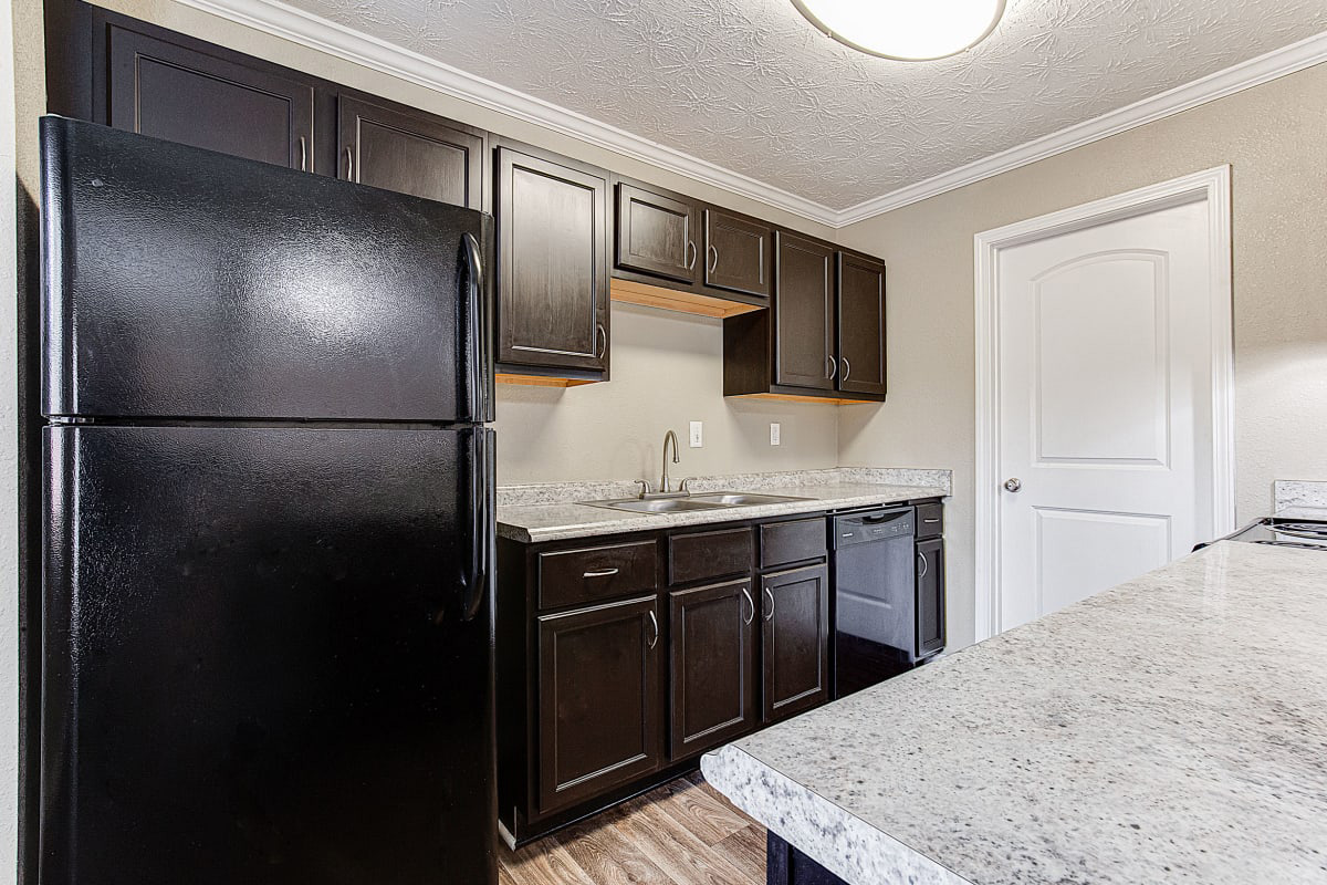 A photograph of a modern kitchen with dark wood cabinets, stainless steel appliances including a refrigerator and oven, granite countertops, and a marble-topped island.